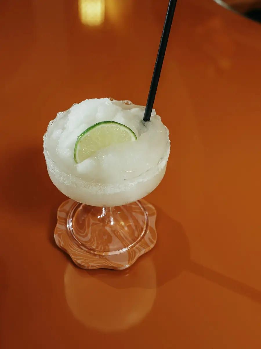 A frozen margarita with a lime wheel against an orange wall